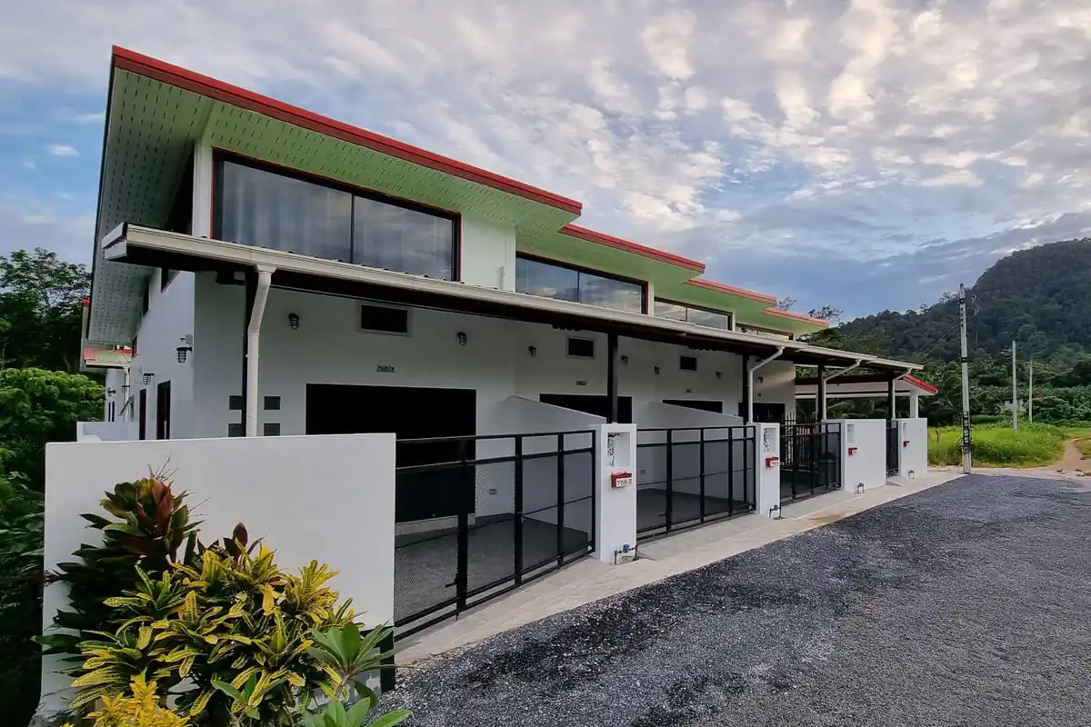 Ao nang valley apartments a terraced row of three modern houses in a private road. all whites are painted white at the front of each is a wide black wire mesh gate opening to a partly covered parking area. Slideing glass doors enter into the small house. They have mezzanine style upper floor. the full width window is under the single slope roof
