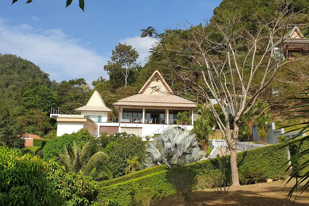 Lanta sunrise villa a modern luxury pool villa on a hillside. Featuring a Lanna Thai style roof. wide feature windows to a balcony and a tropical garden with large palms